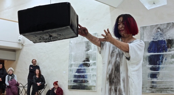 Two blocks of frozen water and two blocks of frozen ink suspended mid-air, drip continuously onto xuan rice paper. Xiao Lu walks towards the first black ice block, caresses it and spins it, moaning softly, letting the black ink drip onto her white dress.
